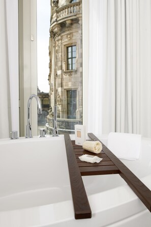 A modern bathroom with a large bathtub, a wooden tray, and a view of a historic building.