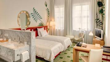 A hotel room with a marble bathroom, two beds, a desk with a computer, and a TV.