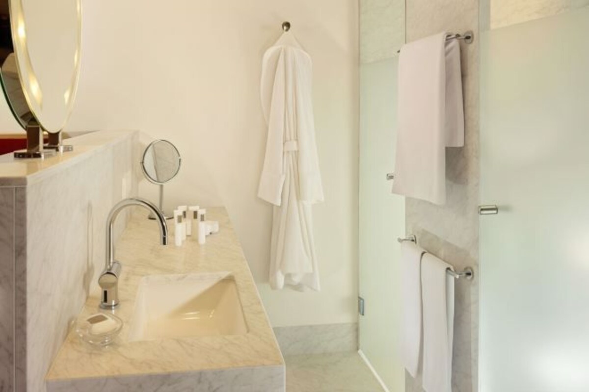 Un baño moderno con lavamanos de mármol, un espejo redondo y cabina de ducha de vidrio.