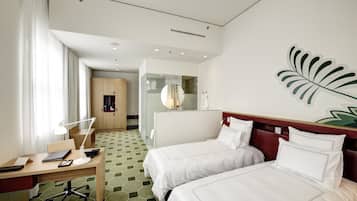 Ein Hotelzimmer mit zwei Betten, einem Schreibtisch mit Stuhl, einer Schreibtischlampe, einem Spiegel und einem großen Blatt-Kunstwerk an der Wand.