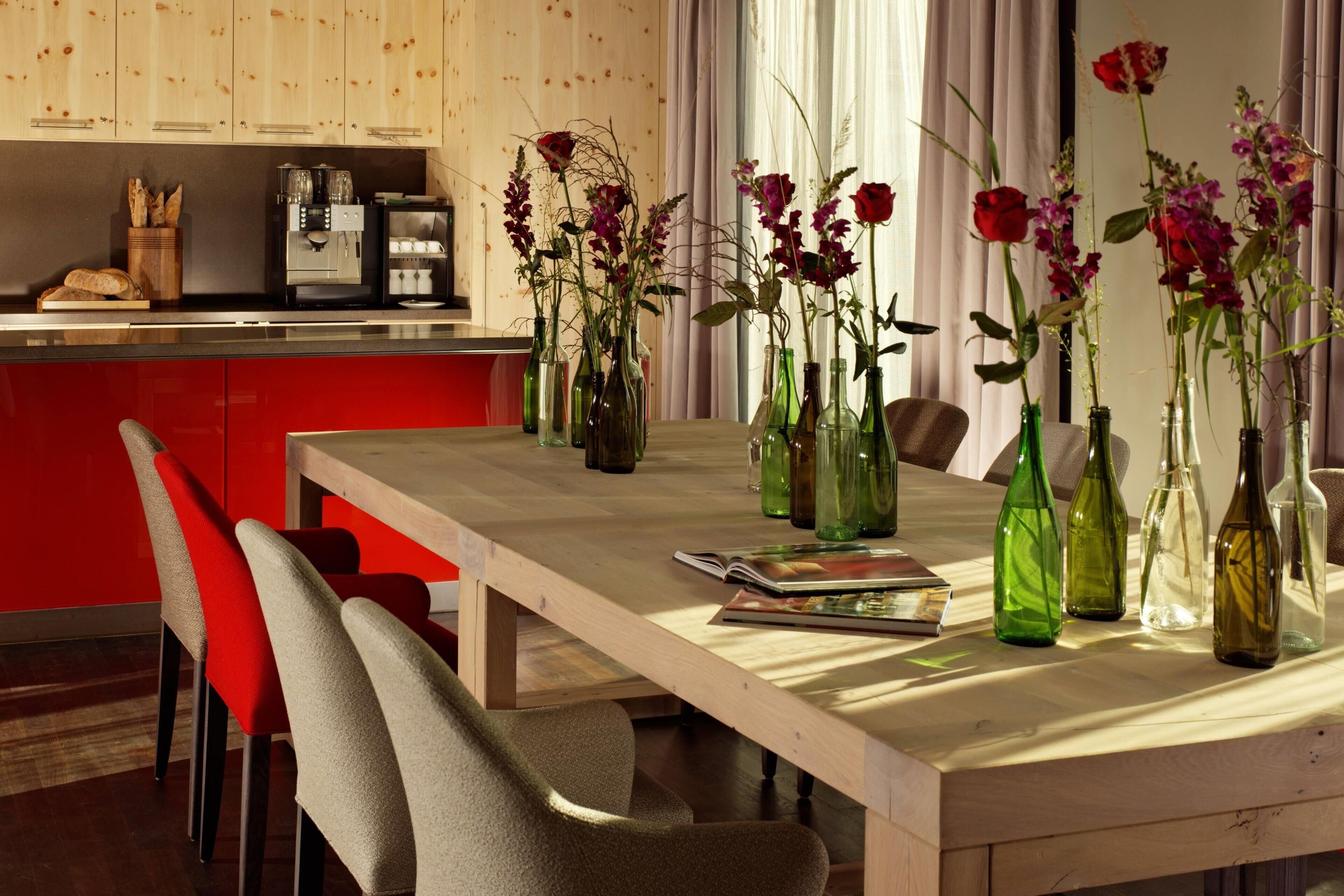 A dining area with a wooden table, chairs, and vases with flowers.