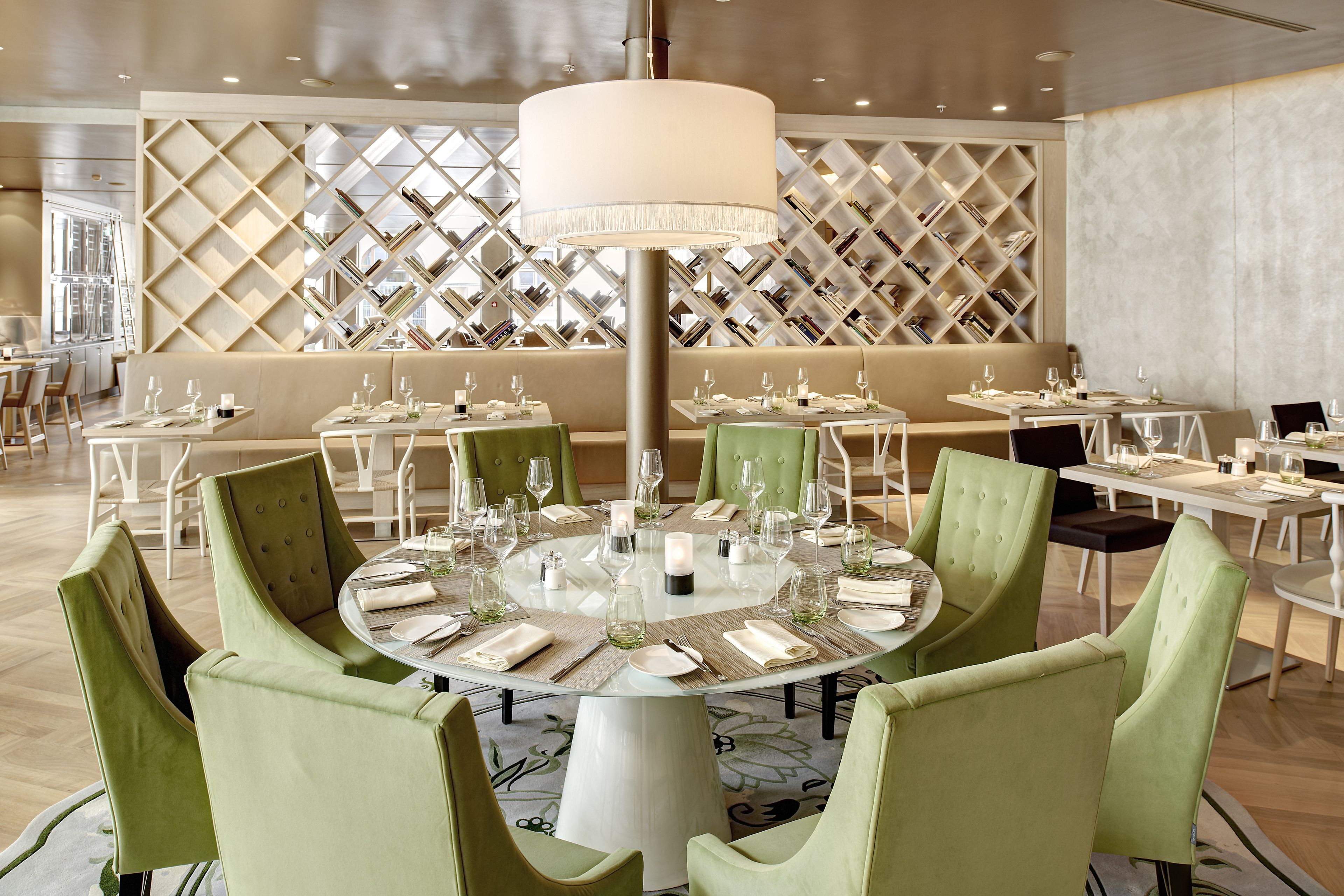A dining area with round tables set for four, surrounded by green upholstered chairs.