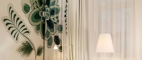 A hotel room with a bed, two armchairs, a desk, and a large floral mural on the wall.