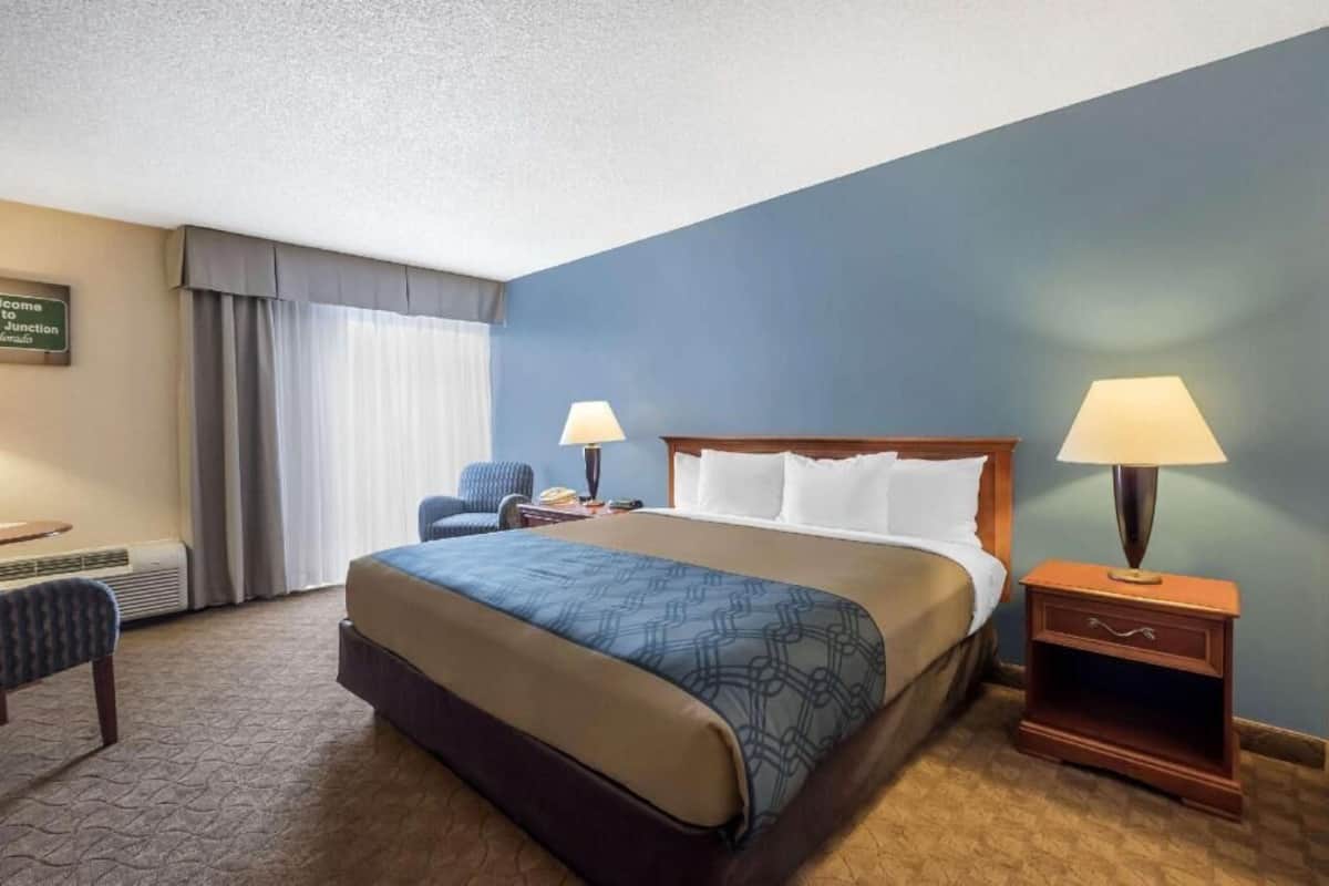 A hotel room with a large bed, two bedside tables with lamps, a chair, a desk, and a sign on the wall.