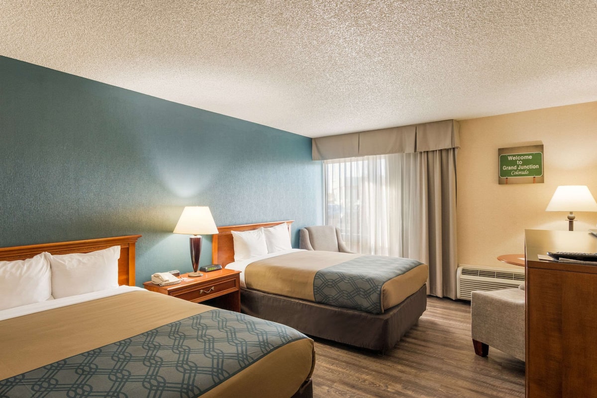 A hotel room with two beds, a desk, a chair, and a sign indicating the location.