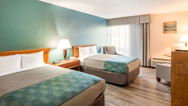 Habitación de hotel con dos camas, un escritorio, una silla y una ventana con cortinas.