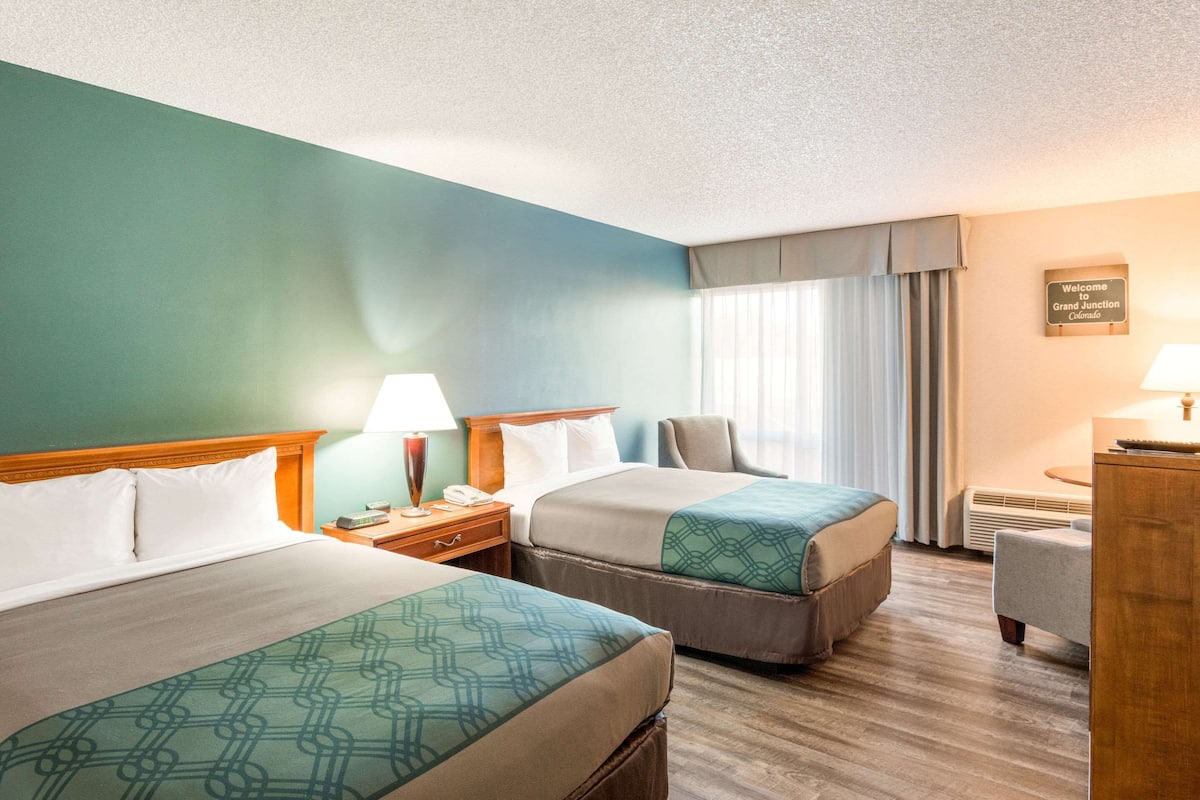 A hotel room with two beds, a desk, a chair, and a window with curtains.