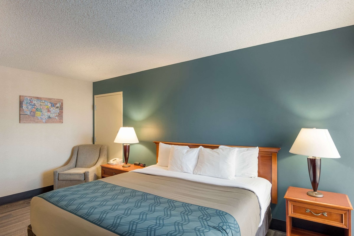 A hotel room with a bed, two bedside tables, a chair, a map on the wall, and a lamp on each table.