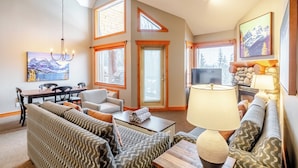 A spacious living room with a high ceiling, large windows, a dining area, and a cozy seating arrangement. - Lizard Creek Lodge (Fernie)