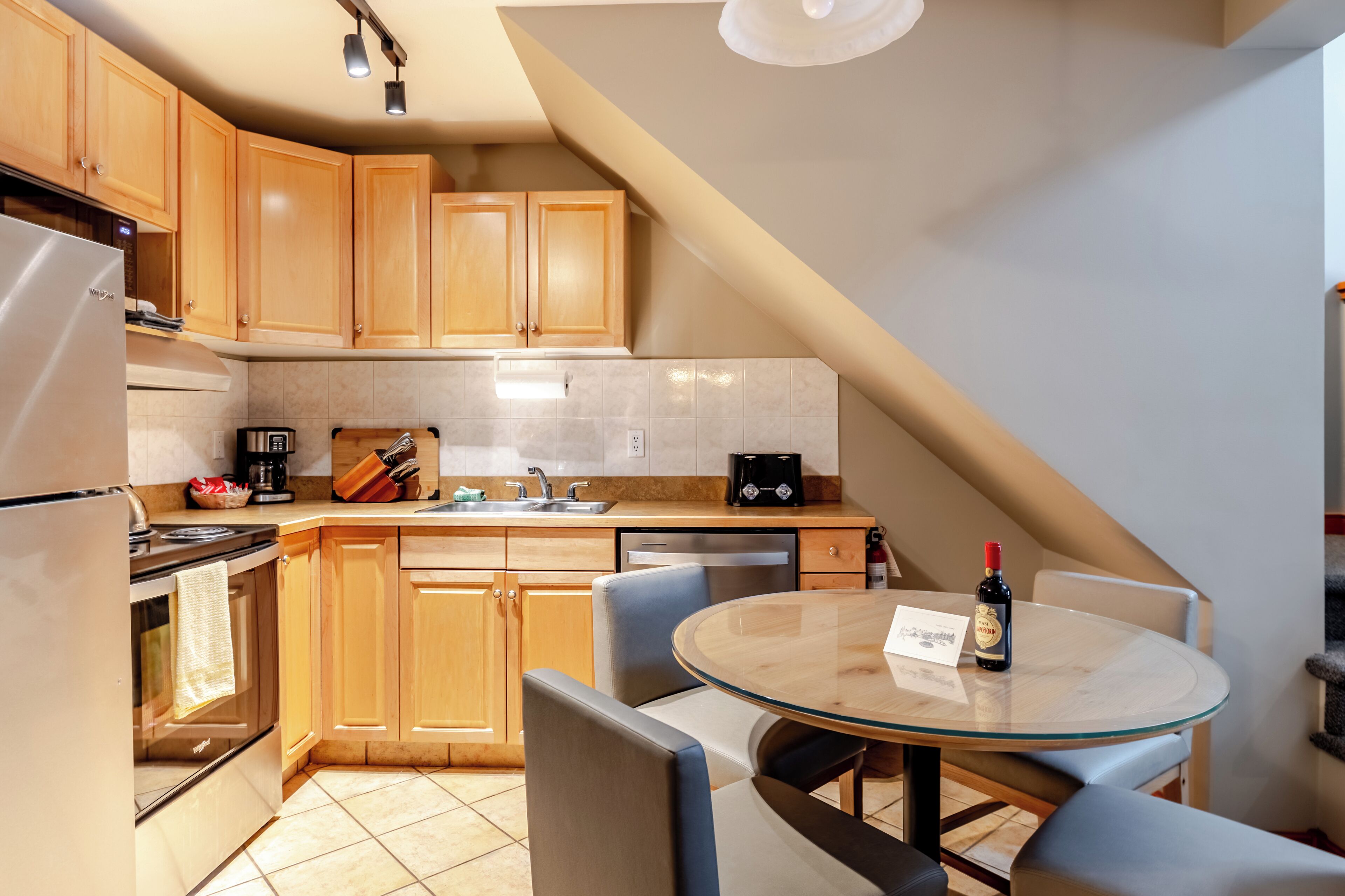 Una cocina moderna con armarios de madera, un refrigerador de acero inoxidable, una cafetera y una botella de vino sobre la encimera.