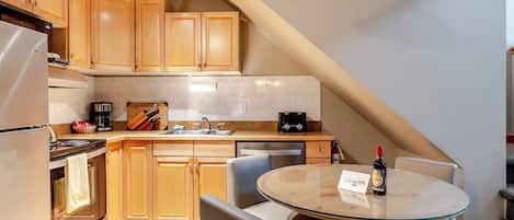Una cocina moderna con armarios de madera, un refrigerador de acero inoxidable, una cafetera y una botella de vino sobre la encimera.