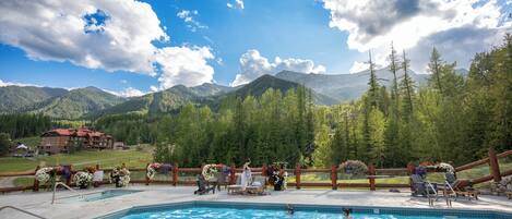 Un espace piscine avec vue sur les montagnes, une clôture en bois et un bâtiment en arrière-plan.