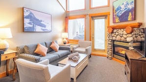 A cozy living room with a fireplace, a couch, a coffee table, and a painting of mountains. - Lizard Creek Lodge (Fernie)