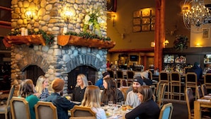 A restaurant with stone walls, wooden furniture, and a fireplace. - Lizard Creek Lodge (Fernie)