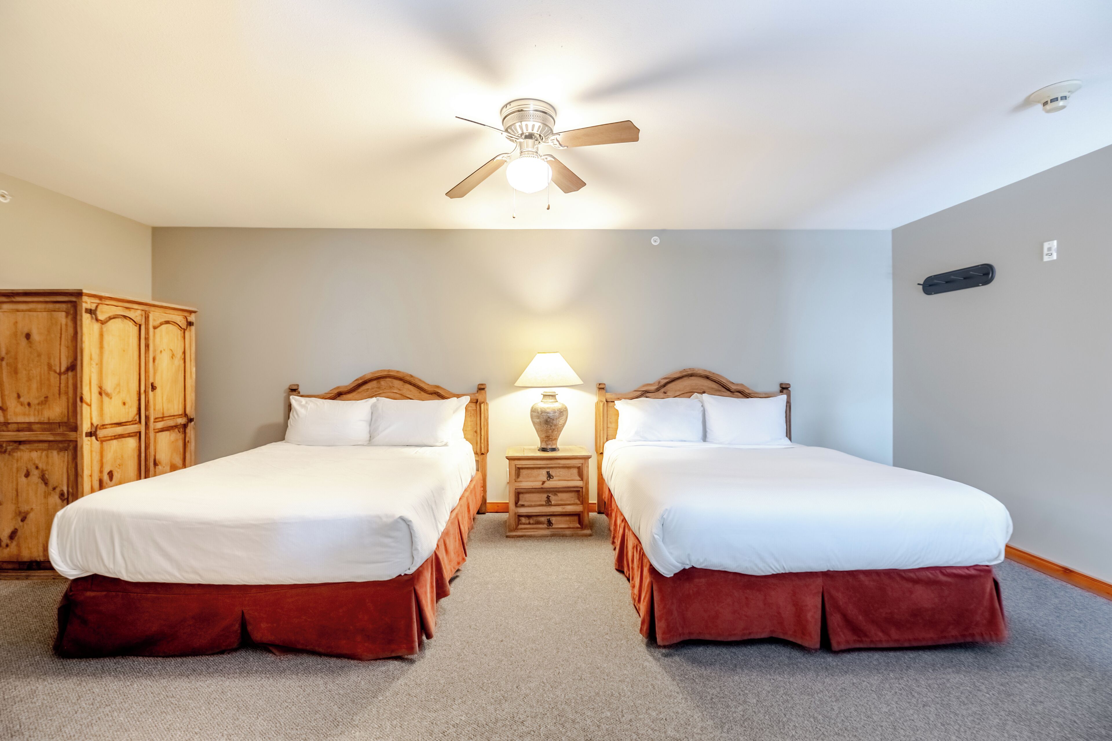 A double room with two beds, a ceiling fan, a nightstand with a lamp, and a wooden wardrobe.