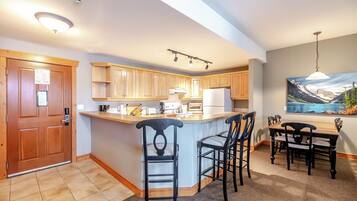 Una cocina moderna con armarios de madera, una isla central con taburetes de bar, una mesa de comedor con sillas y un cuadro en la pared.