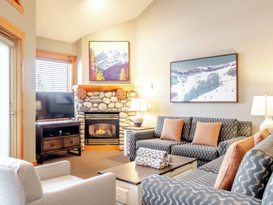 A cozy living room with a stone fireplace, a television, and a large window.