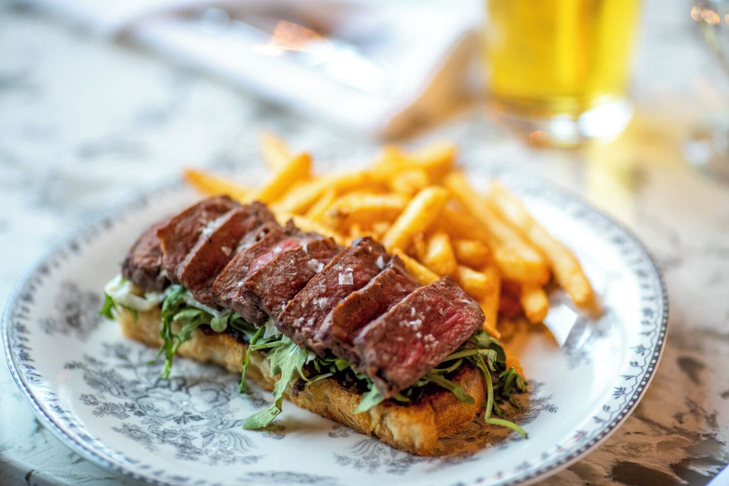 A plate with a steak sandwich and fries.
