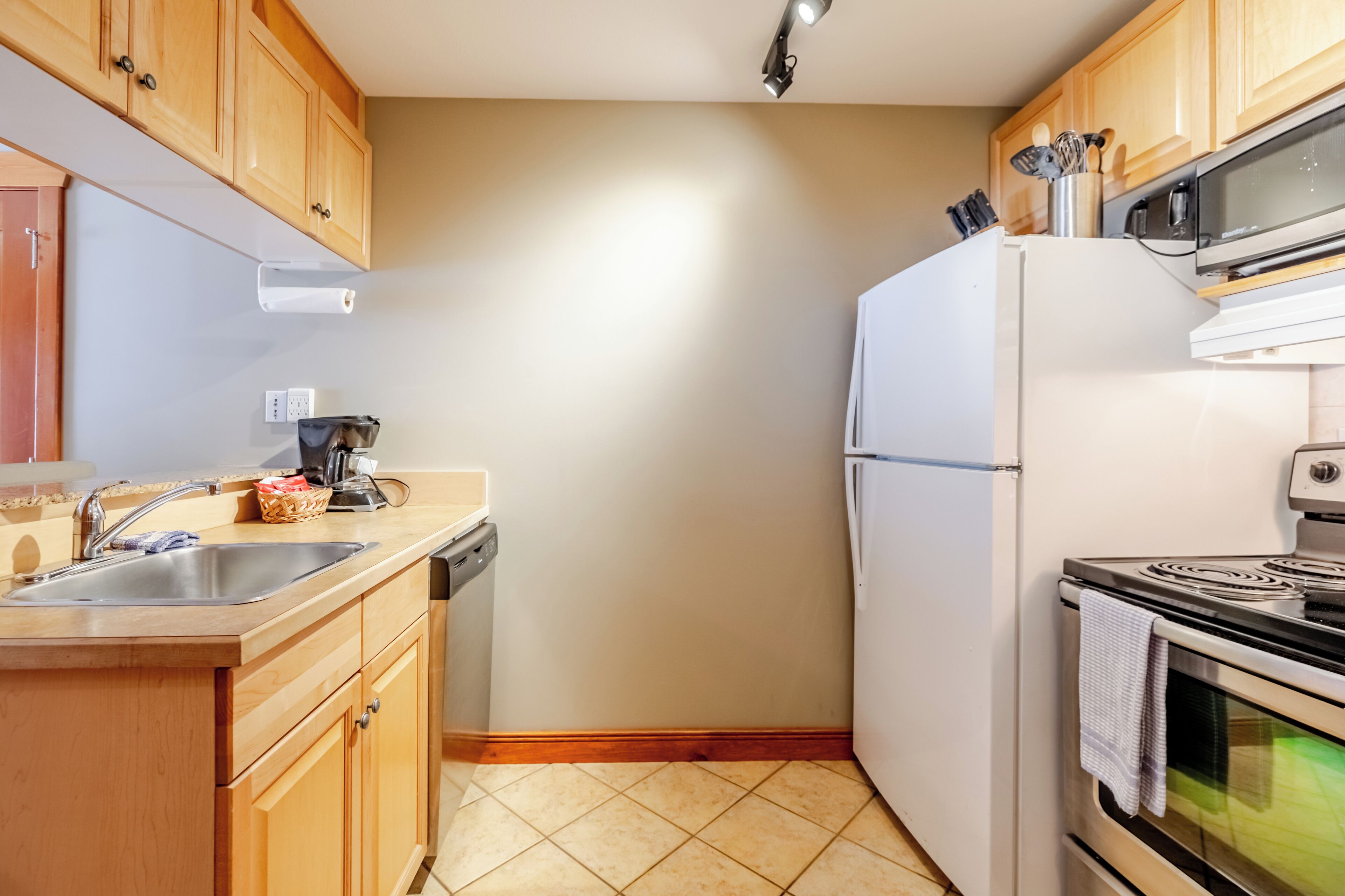 A compact kitchen with wooden cabinets, a white refrigerator, a microwave, and a stove.
