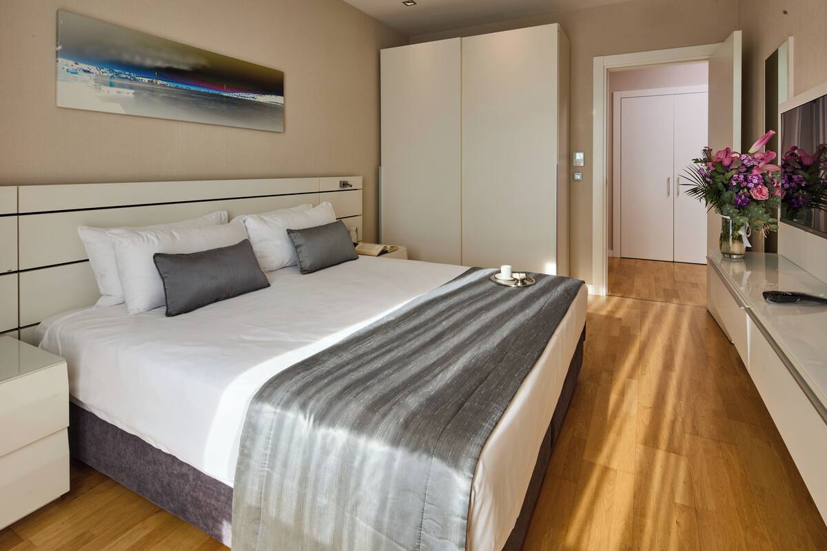 Ein modernes Hotelzimmer mit einem großen Bett, einem Nachttisch, einem Spiegel und einer Vase mit Blumen.