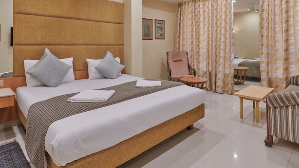 A hotel room with a large bed, a chair, a small table, and a ceiling fan. - Bentley Hotel Marine Drive (Mumbai)