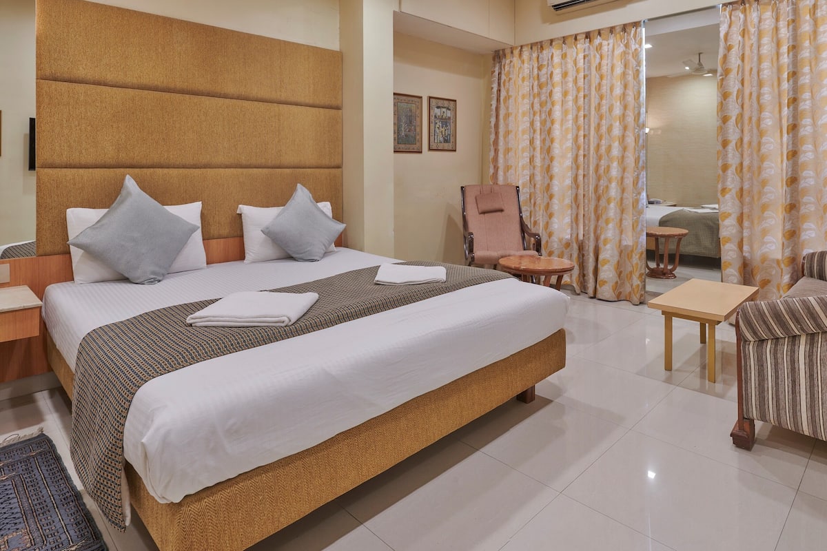 A hotel room with a large bed, a chair, a small table, and a ceiling fan.