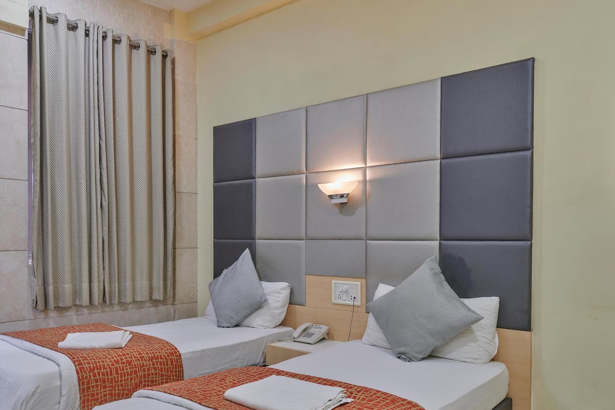 A hotel room with two beds, a large padded headboard, a telephone, and a curtain.
