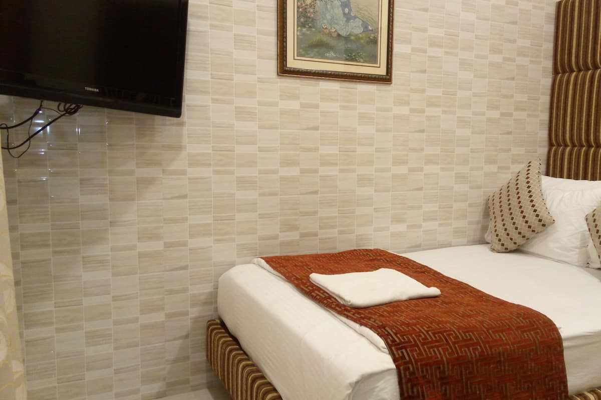 A hotel room with a bed, a television, and a framed picture on the wall.