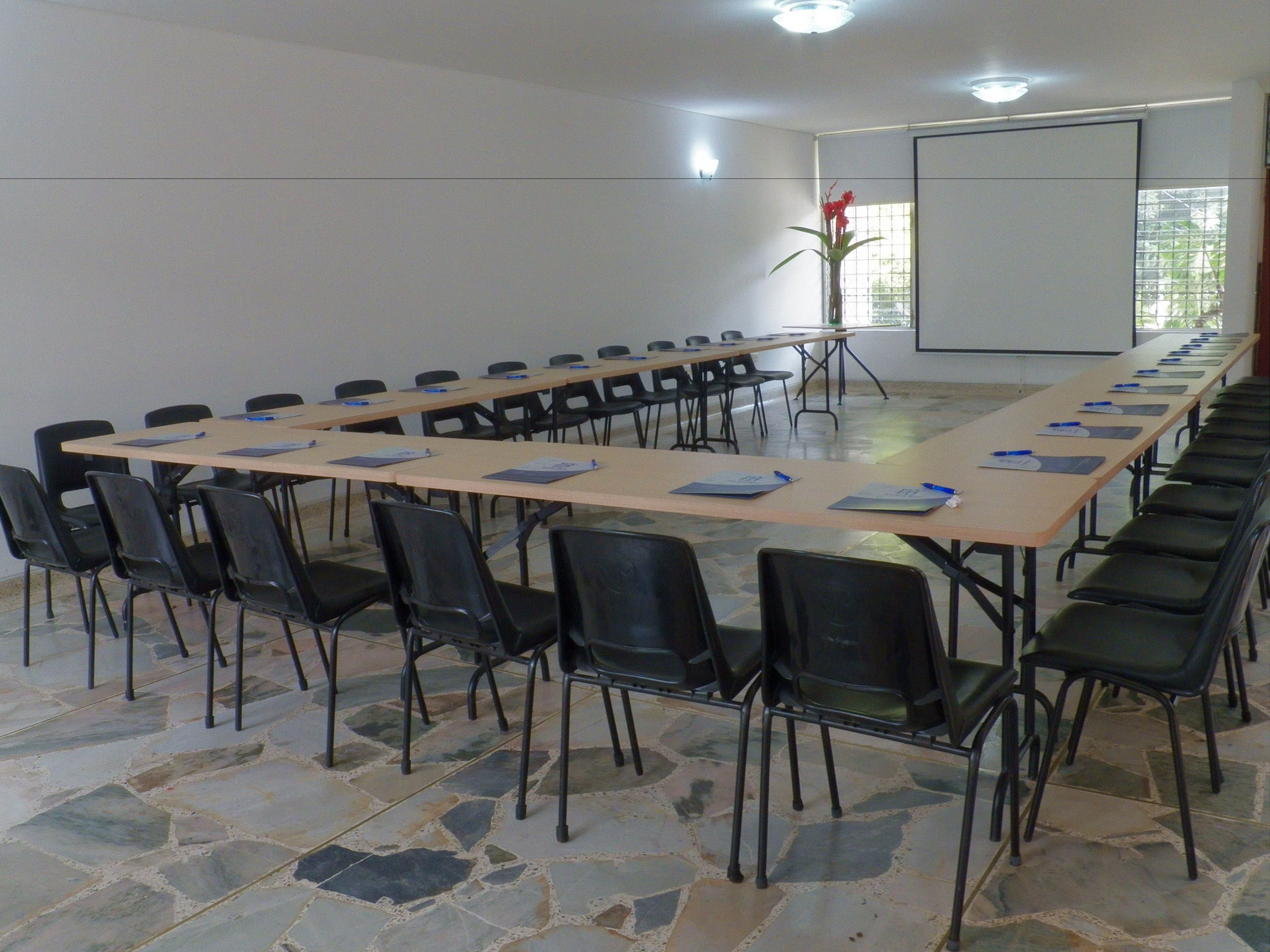 Een vergaderzaal met een lange tafel, stoelen en een projectiescherm.