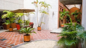 An outdoor patio area with brick flooring, potted plants, and a table with chairs under an umbrella.