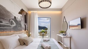 A modern hotel room with a large bed, a view of the outdoors, a small table with a vase of flowers, and a mounted TV. - Sofia Hotel (Agios Vasileios)