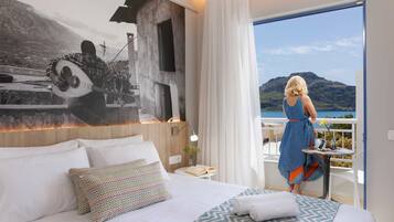 Ein Hotelzimmer mit Bett, Nachttisch, Fenster mit Bergblick und Balkon mit Tisch und Stühlen.