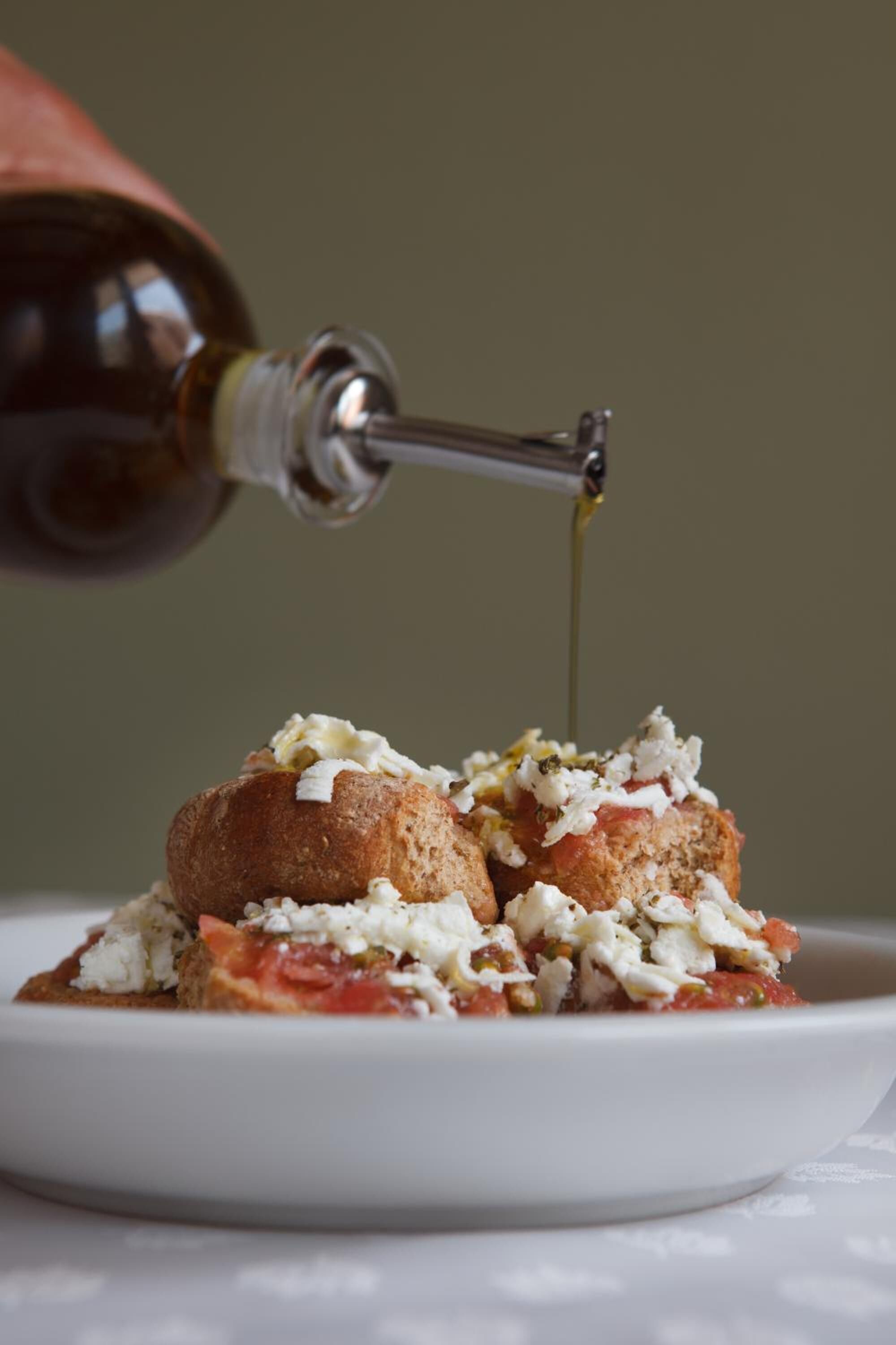 Une assiette blanche sur laquelle se trouve un plat arrosé d’huile d’olive, versée à partir d’une bouteille.