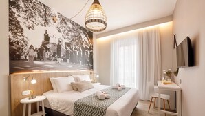 A modern hotel room with a large bed, a bedside table, a desk, and a large wall mural. - Sofia Hotel (Agios Vasileios)