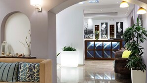 A modern lobby with a reception desk, a large mirror, and a seating area with a sofa and armchairs. - Sofia Hotel (Agios Vasileios)
