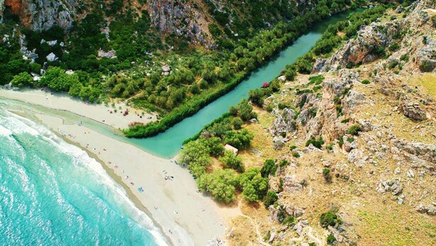 A coastal landscape with a river running through a rocky terrain, a sandy beach, and dense greenery. - Sofia Hotel (Agios Vasileios)