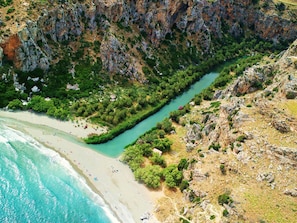 A coastal landscape with a river running through a rocky terrain, a sandy beach, and dense greenery. - Sofia Hotel (Agios Vasileios)