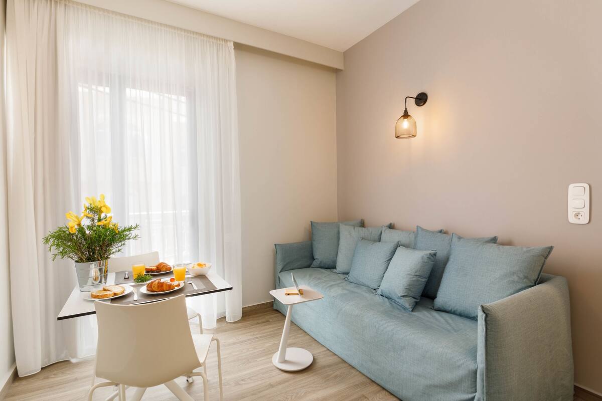 A modern living room with a sofa, a dining table with breakfast, and a wall-mounted light.