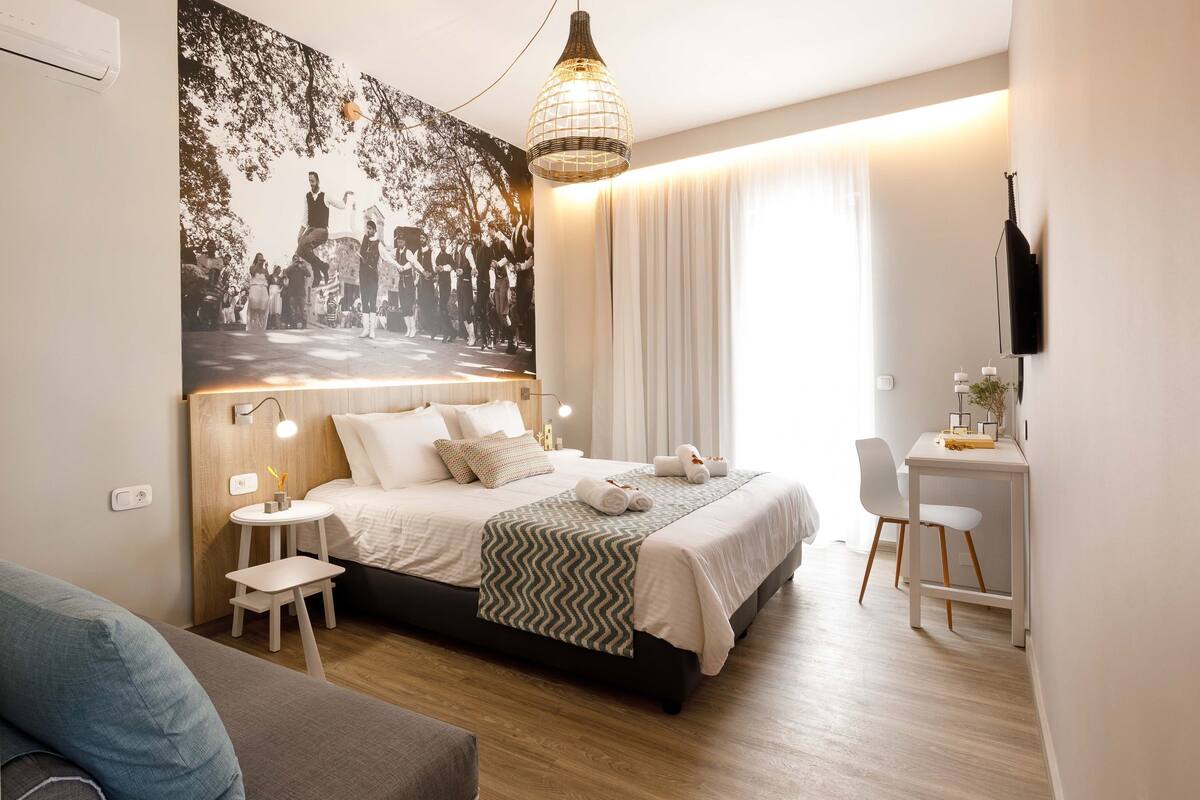 A modern hotel room with a bed, bedside table, lamp, and a desk with a chair.