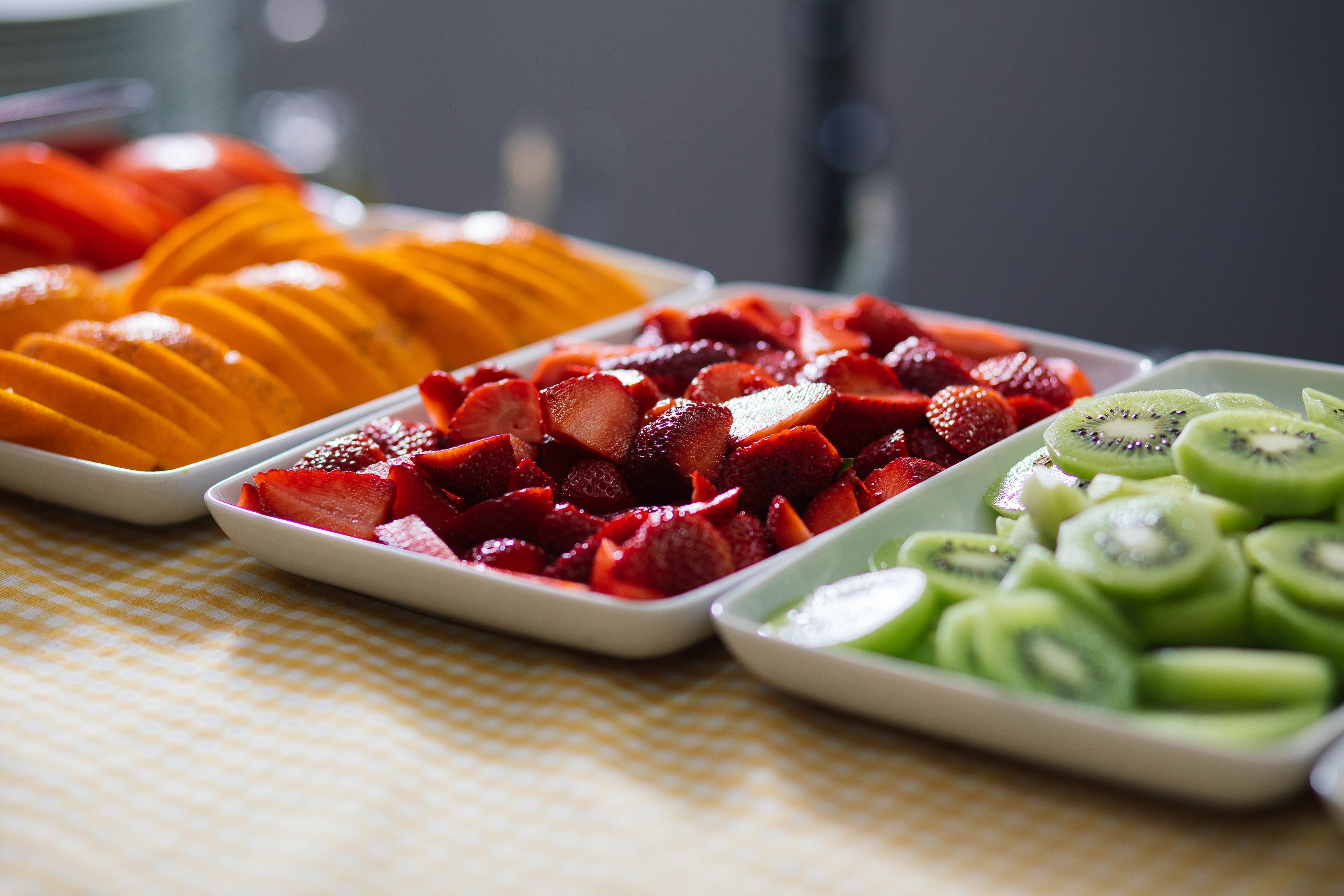 Three trays of sliced fruits on a table.