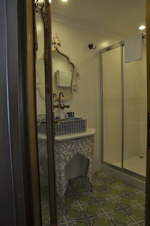 A bathroom with a shower, a sink with a decorative cabinet, and a mirror with an ornate frame. - Kervan Hotel (Istanbul)