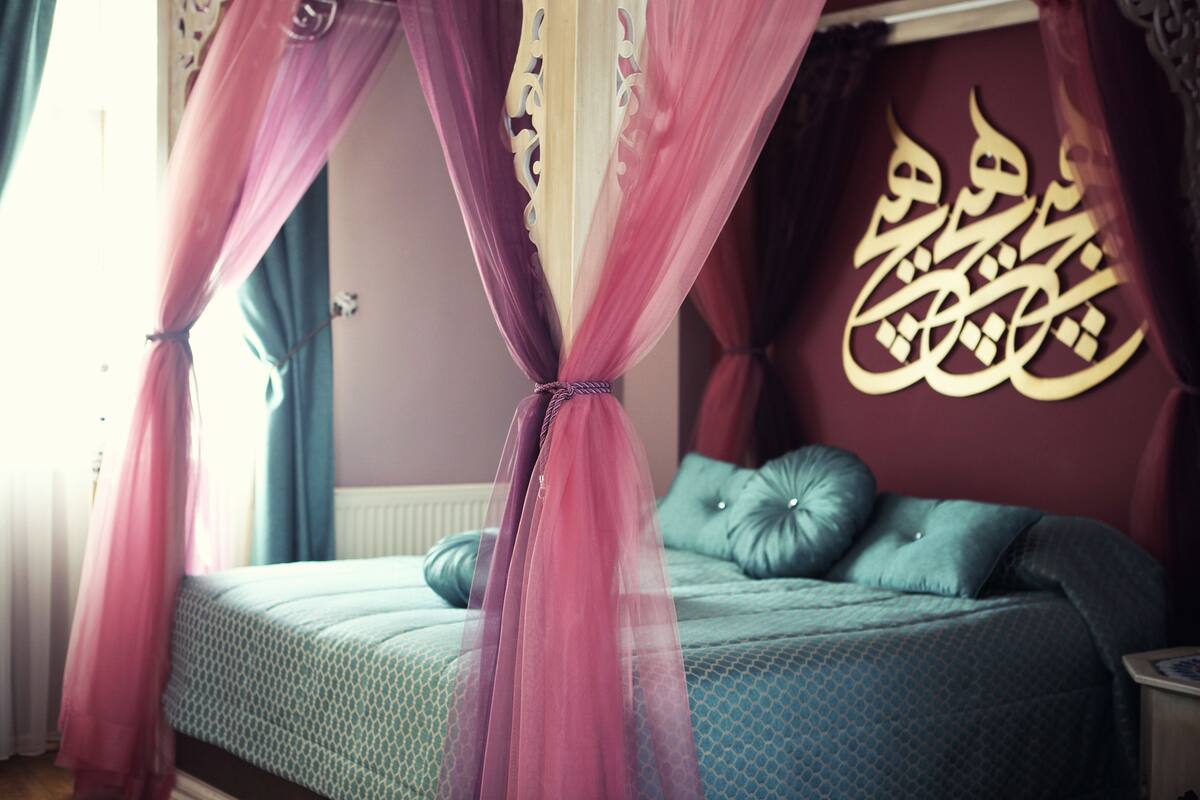 Een slaapkamer met een bed, een hemelbed en een muur met Arabische kalligrafie.