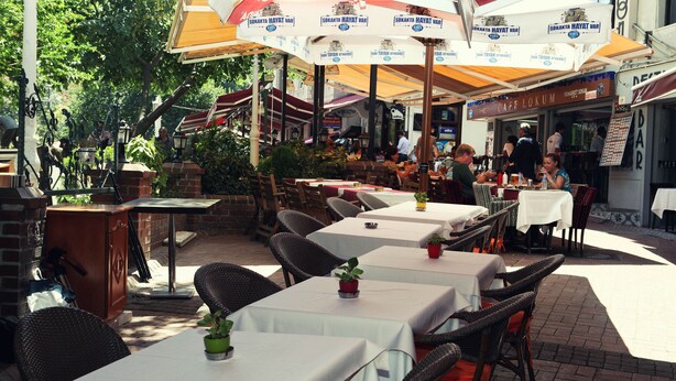 Un café en plein air avec des tables, des chaises, des parasols et un mur en briques.