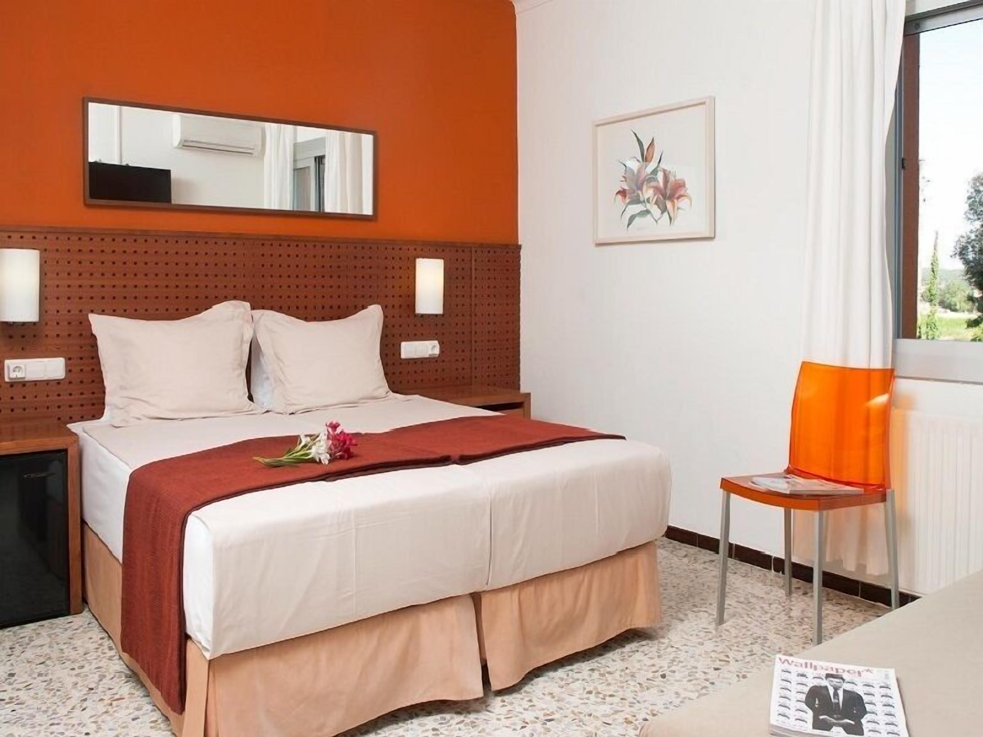A hotel room with a bed, a chair, a mirror, and a window.