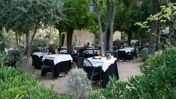 Un área de comedor al aire libre con mesas y sillas, rodeada de árboles y follaje.