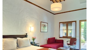 Un dormitorio con una cama grande, un sofá rojo, una mesa de madera y una ventana con cortinas.