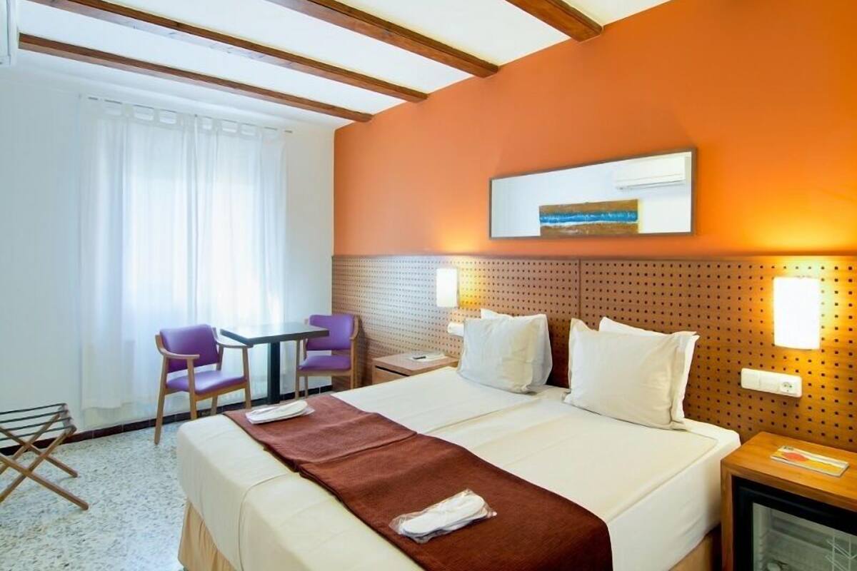 A hotel room with a large bed, a small table with chairs, a desk, and a wall-mounted TV.