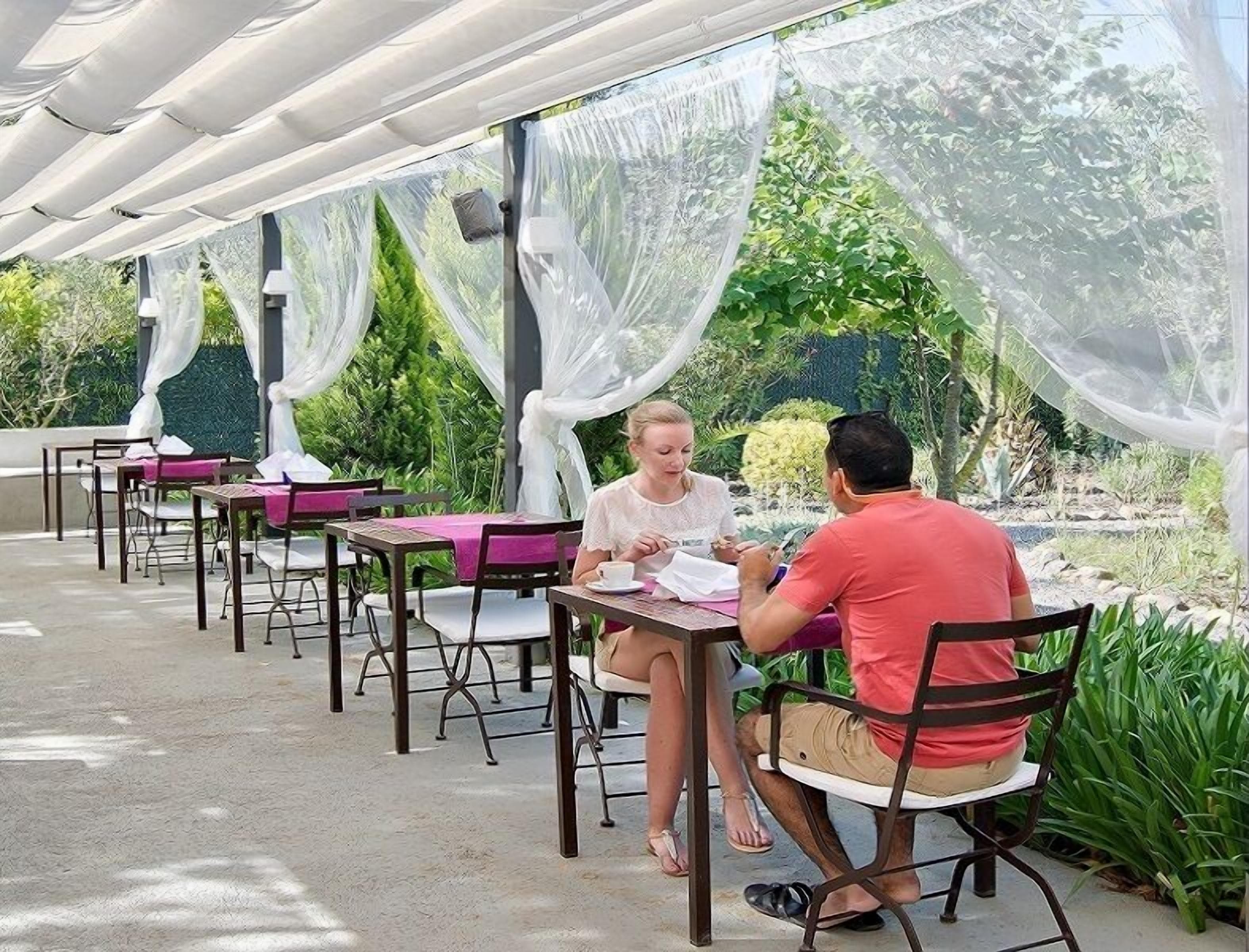 An outdoor seating area with tables and chairs, covered by a white canopy.