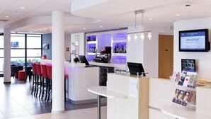 A modern hotel lobby with a reception desk, bar area, and seating. - ibis Lyon Est Chaponnay (Chaponnay)