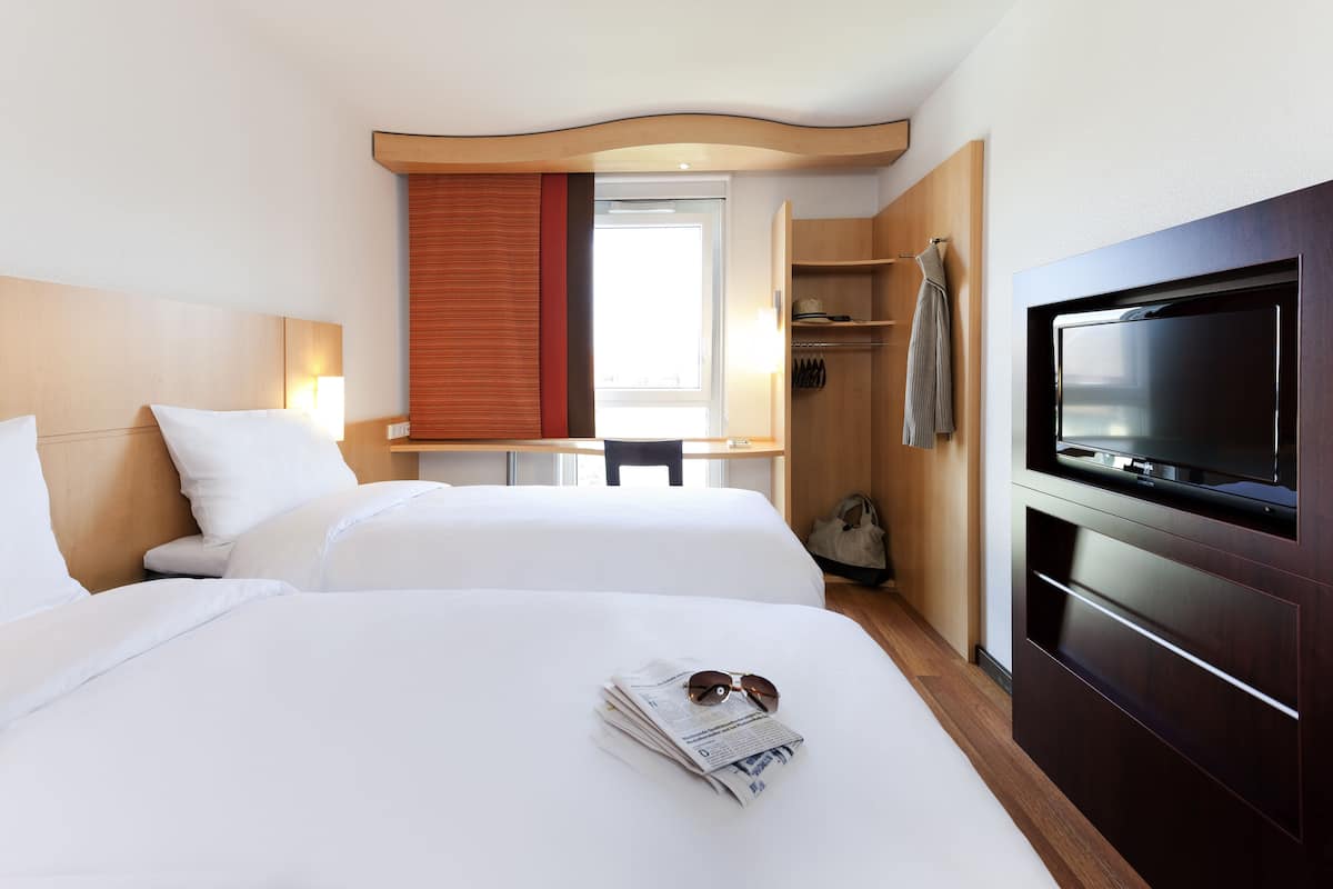 A hotel room with two beds, a TV, a desk, and a wardrobe.